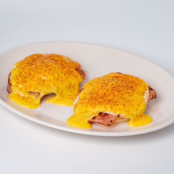 Two eggs Benedict with hollandaise sauce and paprika on a white plate.
