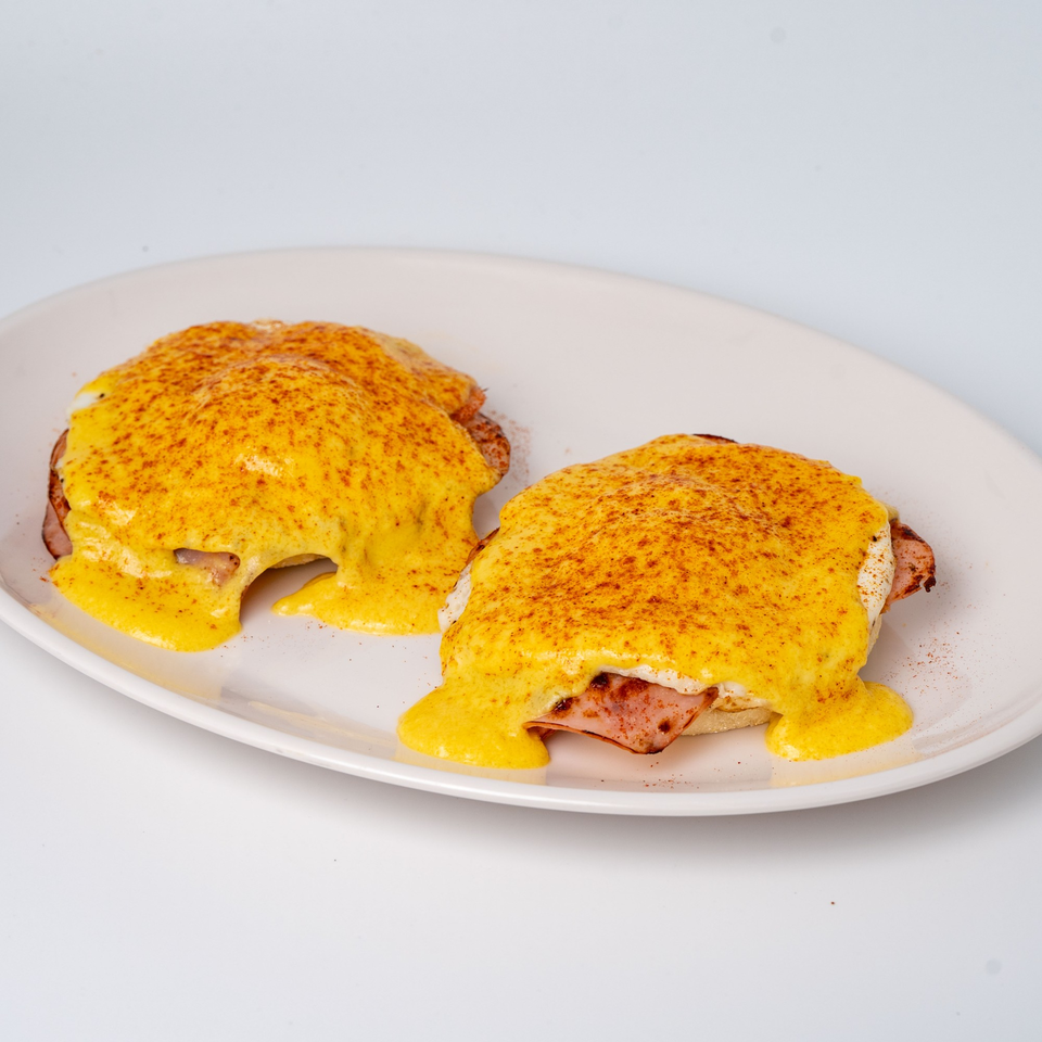 Two eggs Benedict with hollandaise sauce and paprika on a white plate.