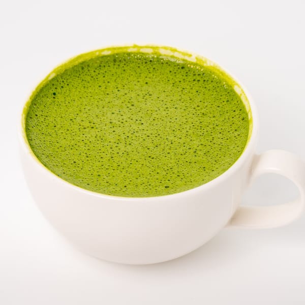 A white mug filled with a vibrant green, frothy matcha latte on a white background.