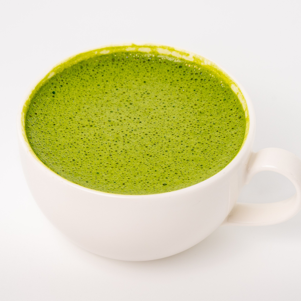 A white mug filled with a vibrant green, frothy matcha latte on a white background.