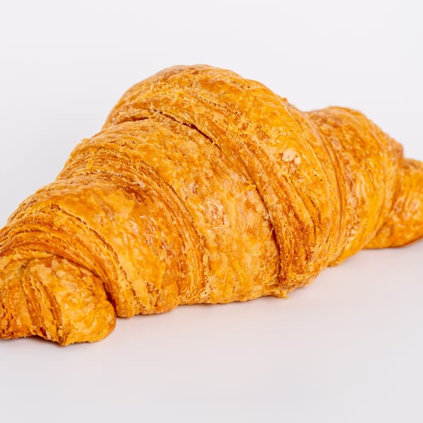 Golden-brown, flaky croissant from Jim & Patty's Coffee, isolated on a white background.