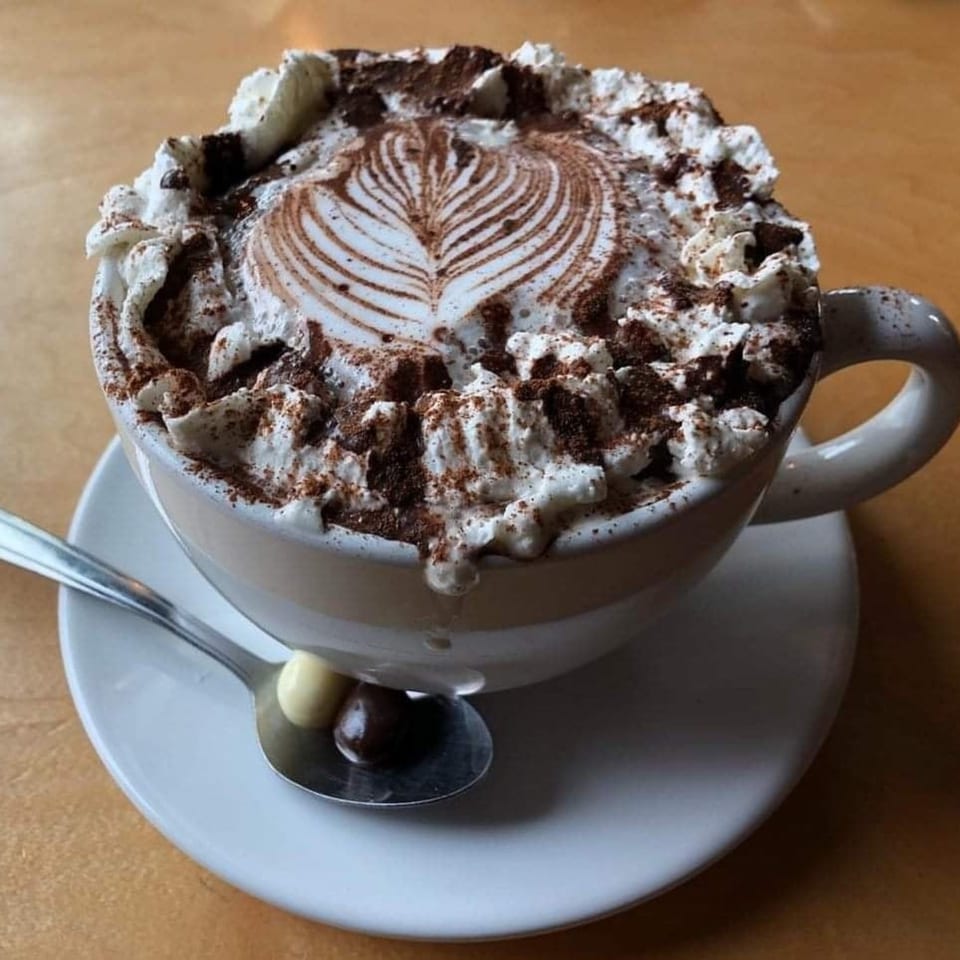 A Jim & Patty's coffee drink with whipped cream, cocoa powder, and latte art.