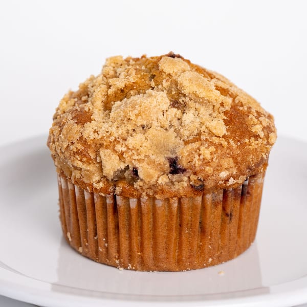 A Jim & Patty's Coffee blueberry muffin with a crumb topping sits on a white plate.